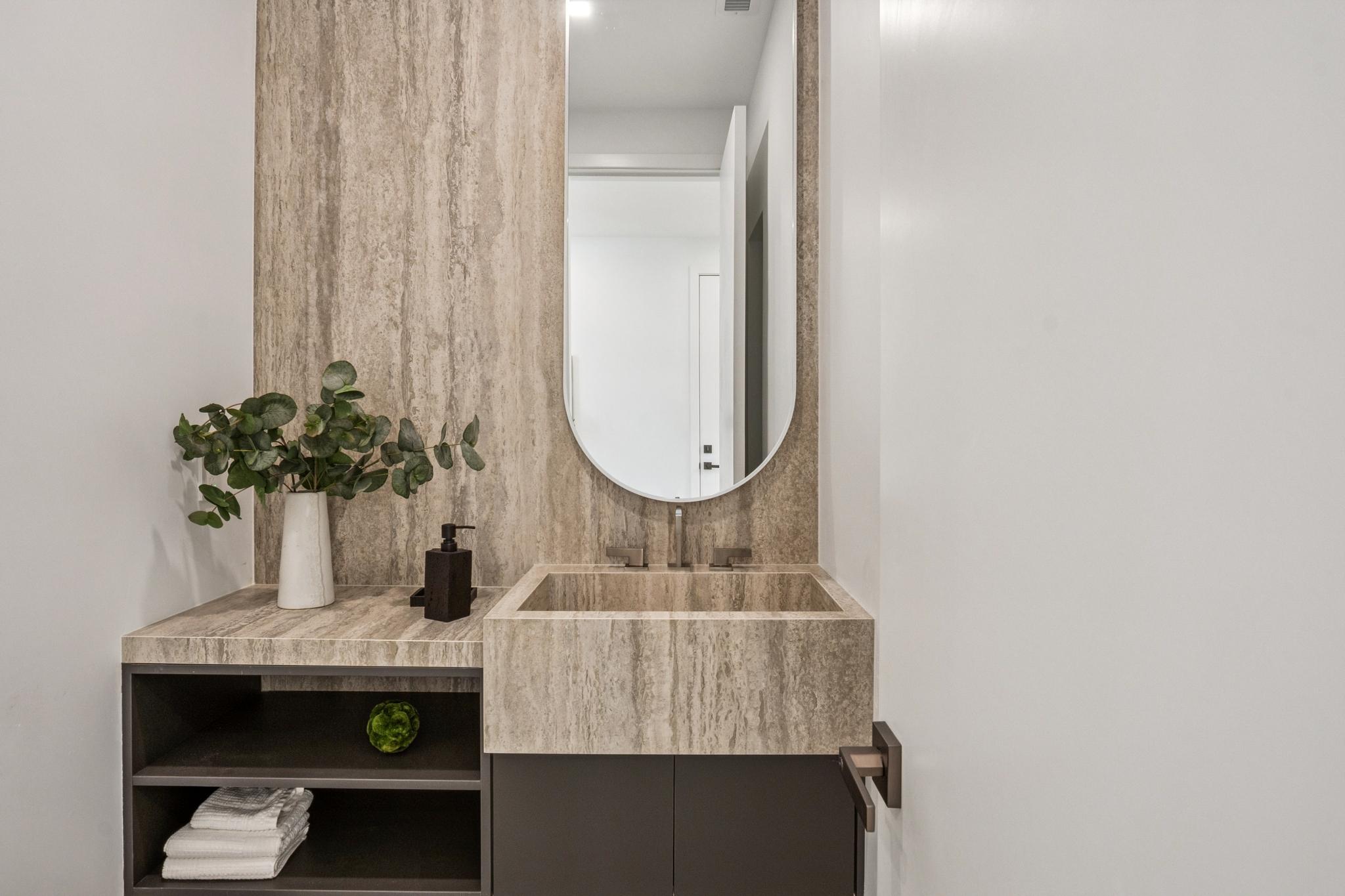 Exquisite luxury powder room in a Willow Glen custom home, featuring a monolithic stone floating sink basin, full-height stone accent walls, and an integrated LED backlit oval mirror.