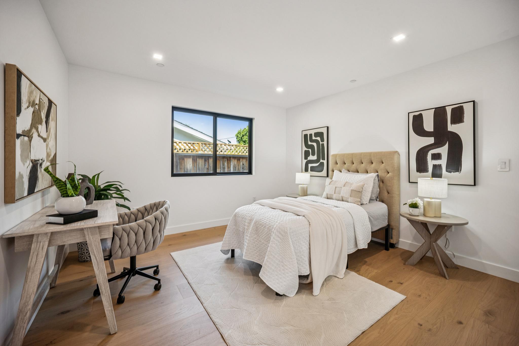 Modern luxury guest bedroom and home office interior in San Jose, showcasing wide-plank European oak flooring, a custom tufted headboard, and abundant natural light designed by Ritz Builders.