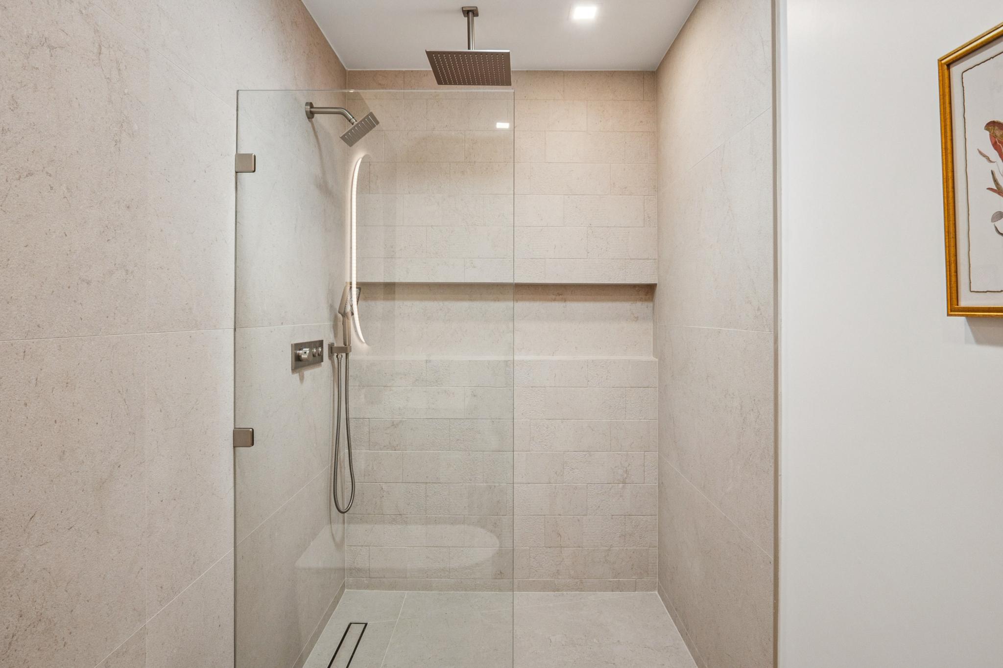 Luxury walk-in shower architecture in Willow Glen, San Jose, featuring frameless glass, textured stone tilework, a modern linear drain, and a premium rain showerhead designed by Ritz Builders.