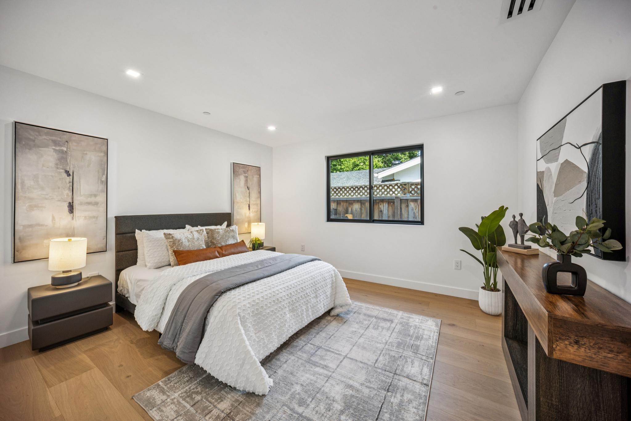 Sophisticated custom bedroom interior in San Jose, displaying a textured upholstered bed, premium wide-plank hardwood floors, and a modern black-framed window overlooking the property by Ritz Builders.