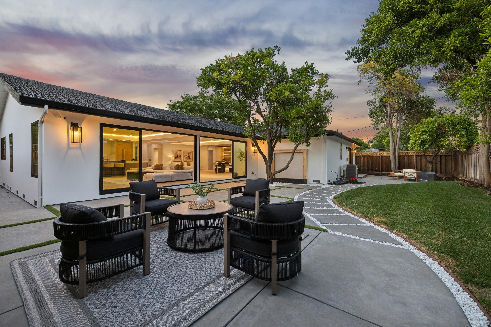 Ultimate indoor-outdoor luxury living space in a San Jose custom home, showcasing a twilight backyard patio with geometric concrete pavers, modern outdoor lounge seating, and expansive sliding glass doors designed by Ritz Builders.