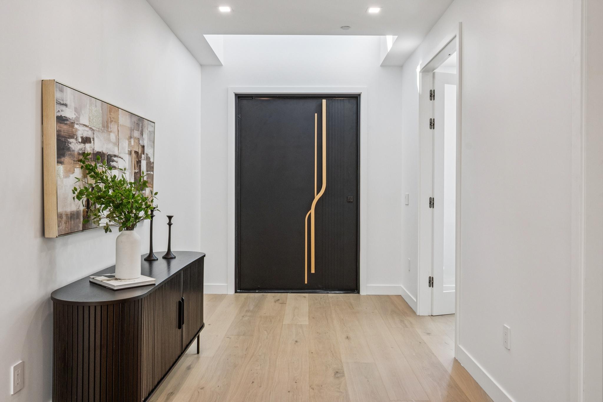 High-end modern foyer interior design featuring an oversized black pivot front door with custom gold hardware lines in a luxury San Jose residence.